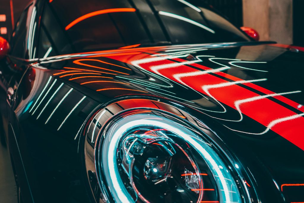 A close-up shot of a glossy black car with neon red lights reflecting off its ceramic-coated surface, highlighting the smooth and polished finish.