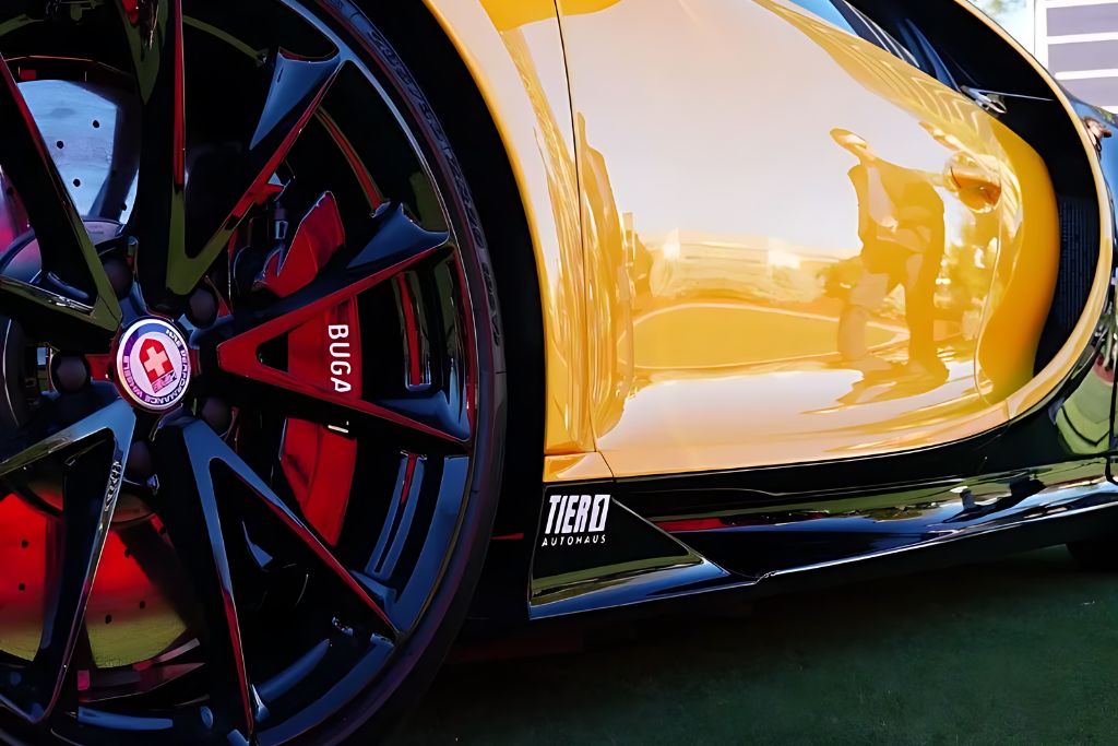 A detailed view of a luxury sports car’s wheel and side panel, showcasing the reflective, high-gloss effect of the ceramic coating. The Tier 1 Autohaus logo is visible on the car's side.